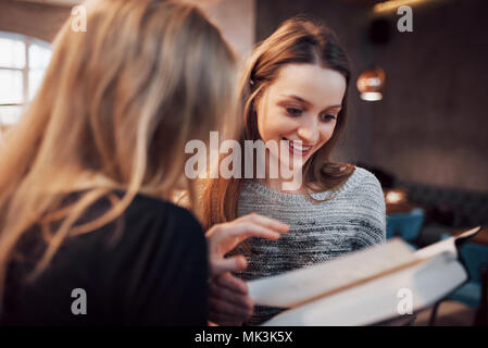 Zwei Mädchen, die in der Lesung buchen Sie während der Pause im Cafe absorbiert. Süße schöne junge Frauen lesen und Kaffee trinken Stockfoto