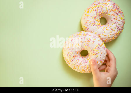 Süß Lecker Snack. kids Hand glasierte Krapfen auf grünem Hintergrund, Ansicht von oben, kopieren. Ungesundes Essen Konzept. Klassiker zwei verglaste Donuts isoliert. Leckere bunte Donuts Stockfoto