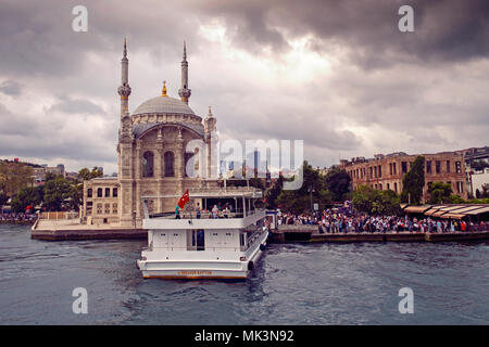 Ein malerischer Blick auf die Ortaköy-Moschee entlang des Bosporus in Istanbul, Türkei, mit einem Passagierboot im Vordergrund. Stockfoto