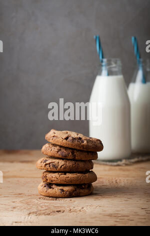 Ein Stapel von Cookies mit Milch Schokolade und zwei Flaschen Milch auf einen hölzernen Tisch. Stockfoto