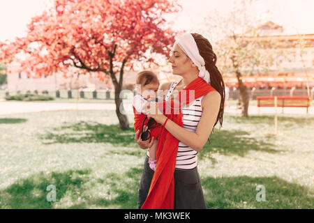 Mutter Kind Baby in wrap Schleuder in Park. Frühling. Konzept der natürlichen parenting glückliche Familie Frühling Konzept Stockfoto