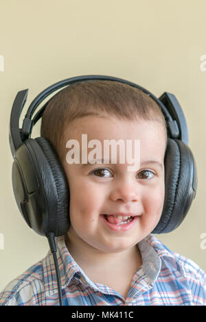 Schönes baby boy im großen Kopfhörer. Ein Junge in einem Plaid Shirt Musik hören. Toddler boy in schwarz Kopfhörer. das Kind in die Kopfhörer lacht. Stockfoto