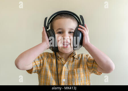 Schönes baby boy im großen Kopfhörer. Ein Junge in einem Plaid Shirt Musik hören. Toddler boy in schwarz Kopfhörer. das Kind in die Kopfhörer lacht. Stockfoto