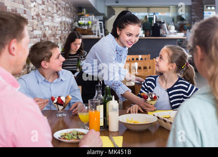 Junge brünette Kellnerin freudige Familie in bequemen Familie Cafe mit Stockfoto