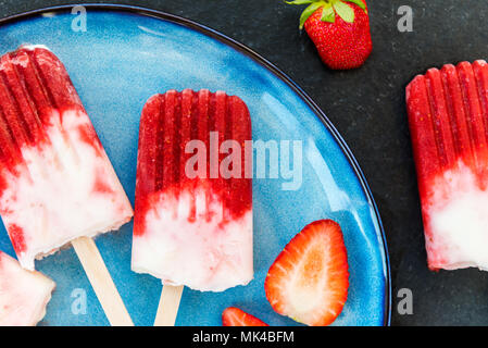 Hausgemachte Vegan Erdbeere Popsicle mit Erdbeersaft und Kokosmilch auf dunklem Marmor Hintergrund. Sommer essen Konzept. Ansicht von oben. Stockfoto