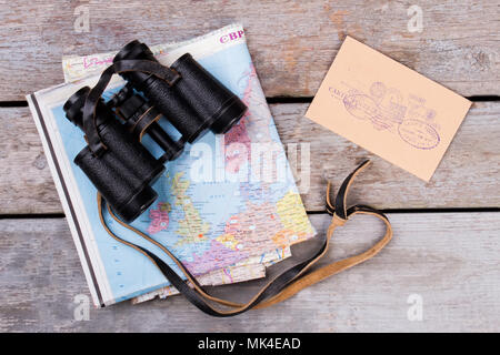 Fernglas auf Karte und Post mit Briefmarken. Ansicht von oben, flach. Schreibtisch aus Holz Oberfläche Hintergrund. Stockfoto