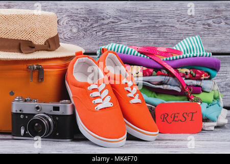 Lenk- und Ruhezeiten outfit Konzept. Frau Kleidung bereit, in Koffer packen. Red sport Sneakers, Foto, Kamera und Stapel der weiblichen Kleidung. Stockfoto