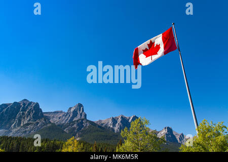 Die roten und weißen Kanadischen Flagge mit einem roten Ahornblatt, Fliegen in einer Brise mit den Rocky Mountains im Hintergrund Stockfoto