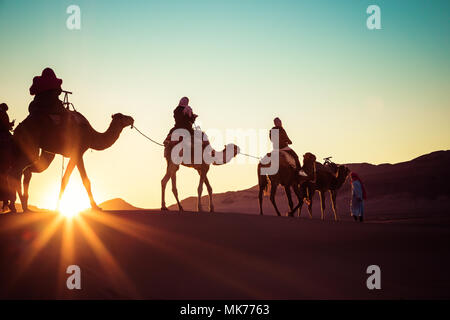 Kamelkarawane mit Menschen, die durch die Sanddünen in der Wüste Sahara. Marokko, Afrika. Stockfoto