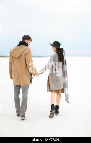 Modische Frau und Mann gehen auf Schnee und halten sich an den Händen und trug Mantel, grau, Schal und Hut. Stockfoto