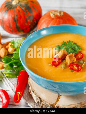 Kürbissuppe mit Chili, Kürbiskerne, Croutons und Petersilie in blaue Schale auf weißem Holz- Hintergrund Stockfoto