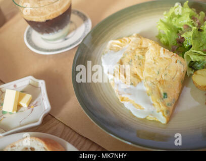 Omelette mit weißen Joghurt Käse, Kartoffeln und Salat in der Keramischen Platte und knusprigen Pommes Scheibe Brot, Butter, Kaffee auf hölzernen Tisch für B Stockfoto