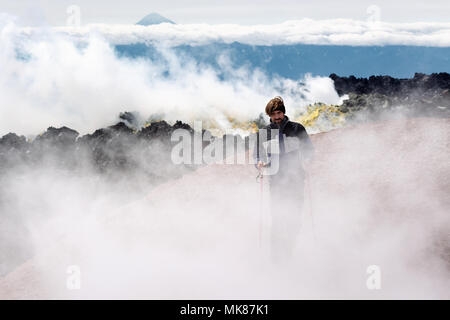 Wanderer klettern auf Lavafeld in Wolken vulkanischer Dampf und Gas in bunten Landschaft Krater des aktiven Vulkans Stockfoto