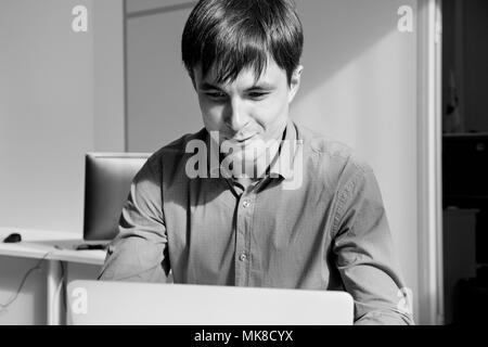 Schwarz-weiß-Porträt einer Smilling Mann vor einem Laptop im Büro. Stockfoto