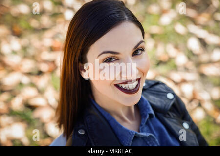 Schöne junge Frau, lächelnd im städtischen Hintergrund. Mädchen mit Lederjacke und blaue T-Shirt Stockfoto