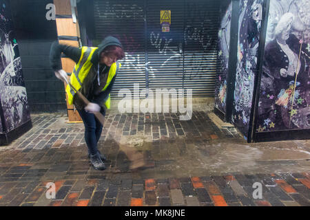 Eine Frau fegt Wasser in einen Abfluss in London Stockfoto