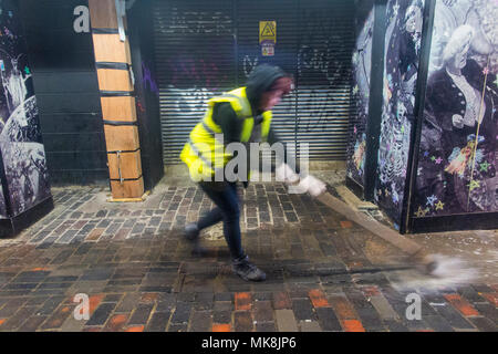 Eine Frau fegt Wasser in einen Abfluss in London Stockfoto