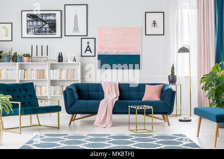 Lampe neben Marine blaue Couch gegen die Wand mit rosa Gemälde und Poster im Wohnzimmer Innenraum Stockfoto