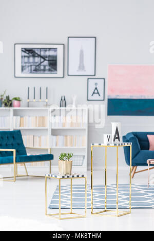 Gold Tisch mit Werk in helles Wohnzimmer Innenraum mit blauen Sessel und Galerie der Poster Stockfoto