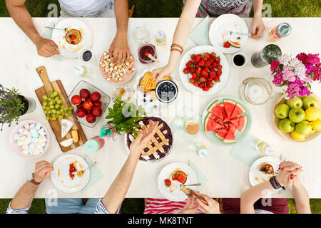 Mixed-Race Gruppe von Studenten draußen sitzen und eine gemeinsame Mahlzeit mit Obst, Waffeln, Wassermelone und Äpfel auf Platten Stockfoto