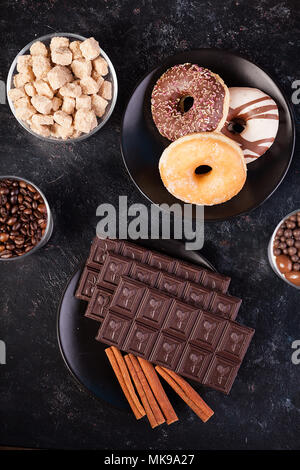 Blick von oben auf die Schokolade Tabletten, Donuts, brauner Zucker mit Erdnüssen in Schokolade und Kaffee Bohnen Stockfoto