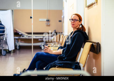 Patient im Krankenhaus Flur sitzen Wartezimmer mit iv. Frau mit intravenösen Therapie in der Hand wartet in der Klinik Flur mit Unschärfe Stockfoto