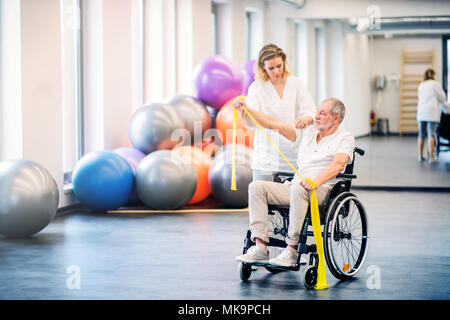 Junge Frau, die Physiotherapeuten arbeiten mit einem älteren Mann im Rollstuhl. Stockfoto