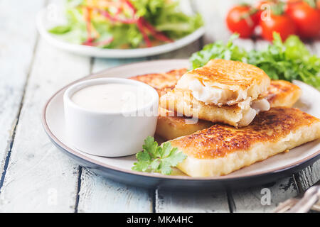 Panierte golden gebratene Fischstäbchen, serviert mit Sauce Tartar und Salat auf einem weißen Holzmöbeln im Landhausstil Hintergrund Stockfoto