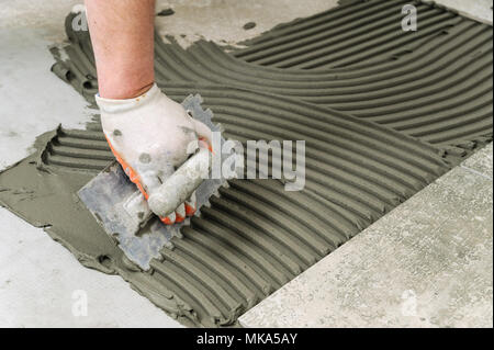 Festlegung von Keramikfliesen. Troweling Mörtel auf Betonboden in der Vorbereitung für die Verlegung von Bodenfliesen. Stockfoto