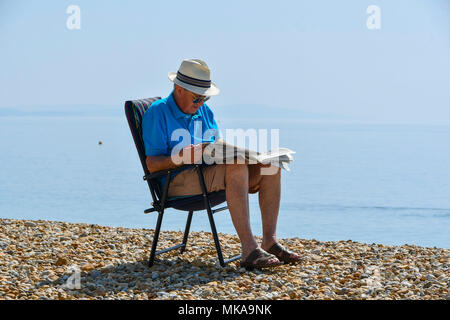 Lyme Regis, Dorset, Großbritannien. 7. Mai 2018. UK Wetter. Ein Mann am Strand eine Zeitung lesen in den Badeort Lyme Regis in Dorset, genießen die heißen sonnigen Feiertag Montag. Foto: Graham Jagd-/Alamy leben Nachrichten Stockfoto