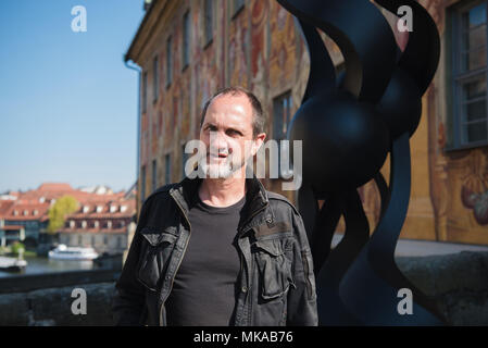 20 April 2018, Deutschland, Bamberg: Der portugiesische Künstler Rui scheuert steht neben der Skulptur "Ich will alles von dir' (lit. Ich will alles von dir) auf der Brücke vor dem Alten Rathaus. Foto: Nicolas Armer/dpa Stockfoto