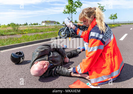 Ein deutscher Sanitäter hilft einem verletzten Motorradfahrer. Rettungsdienst ist das deutsche Wort für Krankenwagen. Stockfoto