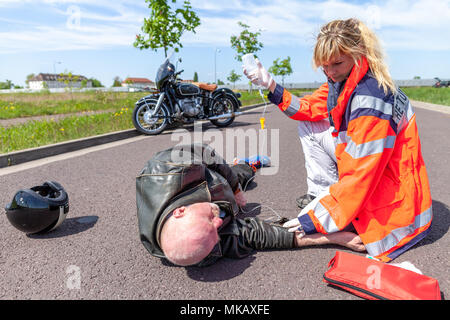 Ein deutscher Sanitäter hilft einem verletzten Motorradfahrer. Rettungsdienst ist das deutsche Wort für Krankenwagen. Stockfoto