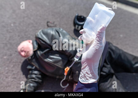 Deutsche Ambulance Service person hält eine Infusion, die in der Nähe von einem verletzten Biker Stockfoto