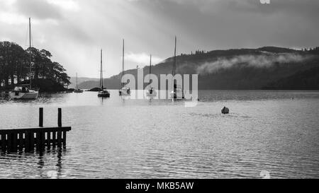 Die Boote sind gegen einen nebligen Herbst Sonnenaufgang am Windermere See in Ambleside in England Lake District National Park. Stockfoto