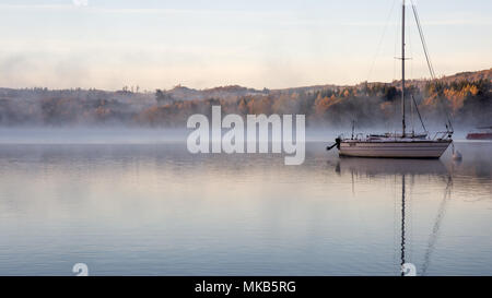 Nebel steigt aus dem ruhigen Wasser des Windermere See um angelegten Boote an der Ambleside Pier in England Lake District National Park. Stockfoto