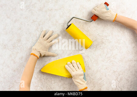 Hände mit Spachtel und Walze Glättung Tapeten an der Wand Stockfoto