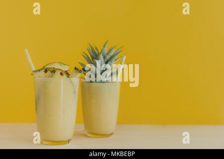 Kristall Gläser gefüllt mit Ananas Smoothie und mit fruchtschnitten auf gelbem Hintergrund eingerichtet. Stockfoto