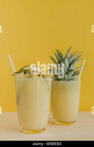 Kristall Gläser gefüllt mit Ananas Smoothie und mit fruchtschnitten auf gelbem Hintergrund eingerichtet. Stockfoto