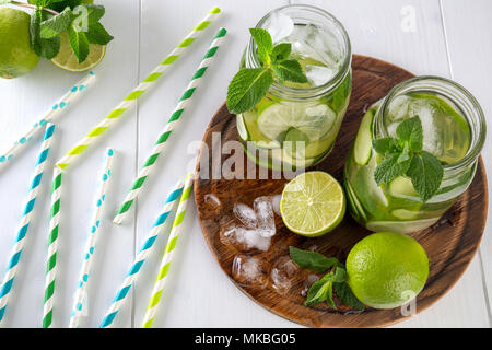 Zwei Gläser von Obst und Kräuter infundiert Wasser mit Gurke, Limette, Minze und Eis Stücke auf einem Holzbrett. Cocktail Papierrollen werden auf einem Tisch verteilt. Th Stockfoto