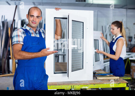 Sorgfältige positive zuversichtlich Mann in Arbeitskleidung mit fertigen Fenster aus PVC-Profil am Arbeitsplatz Stockfoto