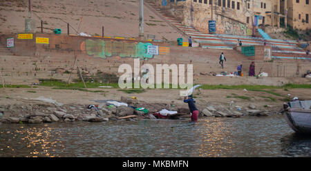 Ein einsamer laundryman verwendet einen flachen Stein die Wäsche Schlag gegen so wäscht er es in den Ganges in Varanasi. Stockfoto