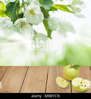 Reifen Apfel Früchte auf Braun leer Holztisch gegen Abstrakt Hintergrund mit grünen Blättern und weißen Blüten Stockfoto