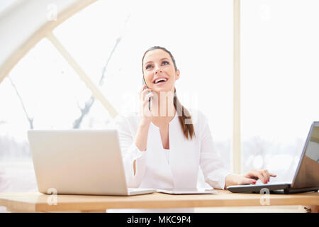 Glückliche junge geschäftsfrau mit Handy und Beratung mit Ihrem Kunden während der Sitzung in der Vorderseite des Laptops im Büro. Multitasking. Stockfoto