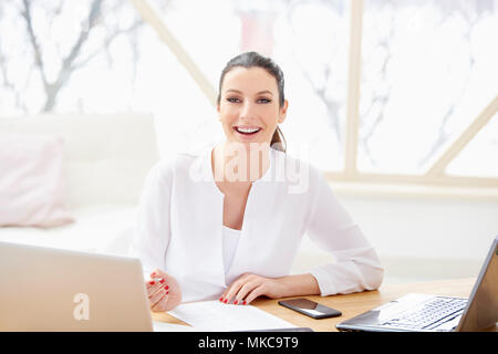Lächelnd vertrieb Frau dabei einige Unterlagen im Büro sitzend vor Laptop im Büro. Stockfoto