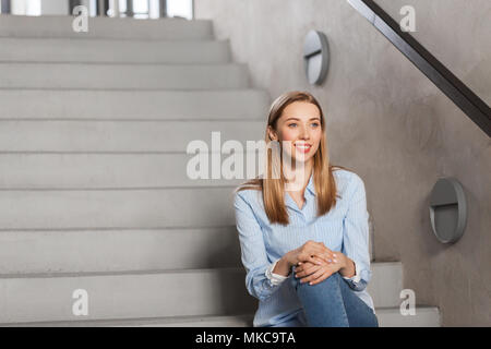 Glücklich lächelnde Frau oder ein Schüler sitzt auf der Treppe Stockfoto