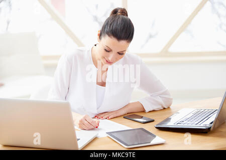 Lächelnd vertrieb Frau dabei einige Unterlagen im Büro sitzend vor Laptop im Büro. Stockfoto