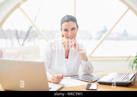 Lächelnd vertrieb Frau dabei einige Unterlagen im Büro sitzend vor Laptop im Büro. Stockfoto