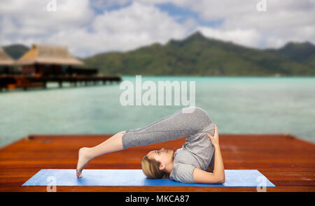 Frau macht Yoga im Pflug-Pose auf Matte im freien Stockfoto