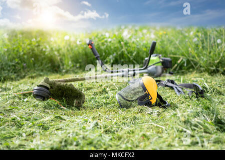 String Trimmer und schützende Maske auf gemähten Gras, Gras und den blauen Himmel im Hintergrund, Sonnenlicht Stockfoto